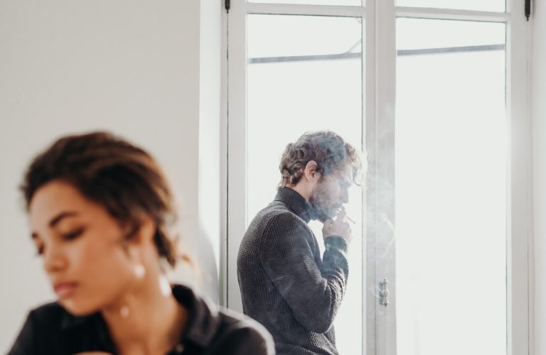 man standing near window smoking at a support circle for domestic violence and substance abuse