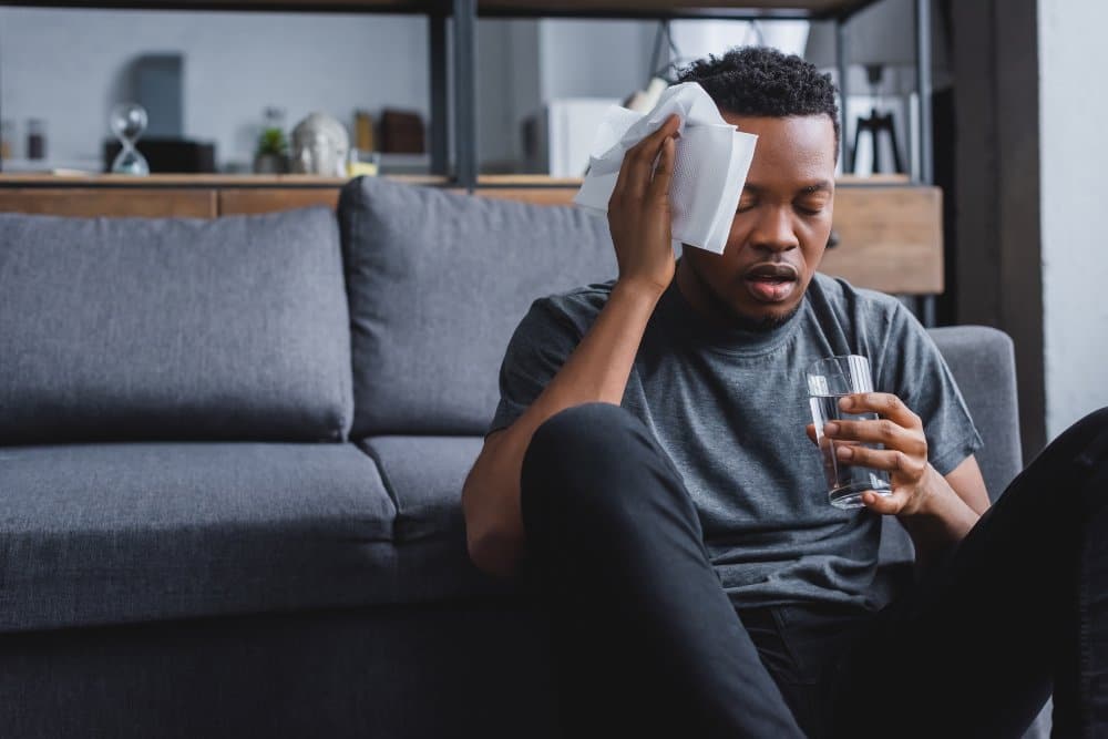sweaty african american man holding glass of water and napkins after panic attack at home
