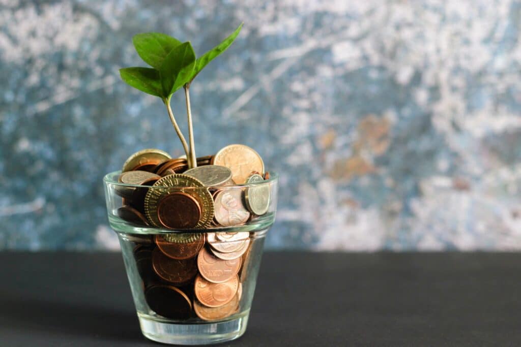 a glass cup filled with coins and a plant growing out of it