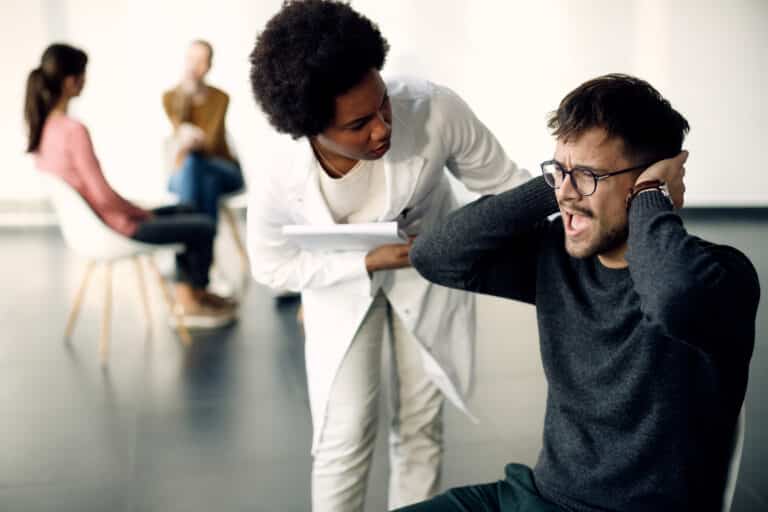 Anxious man covering his ears and screaming while psychotherapist is trying to talking to his during group therapy. Oppositional Defiant Disorder vs. Conduct Disorder.