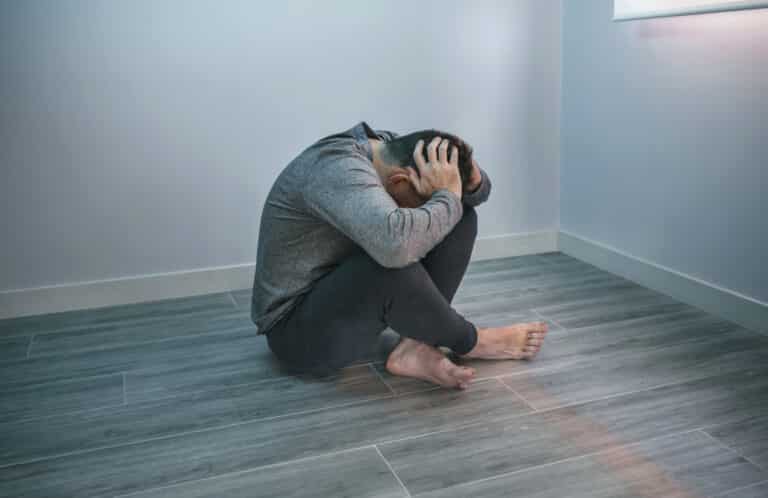 Unrecognizable man with problems holding his head with hands sitting on the floor. He has OCD and Trauma