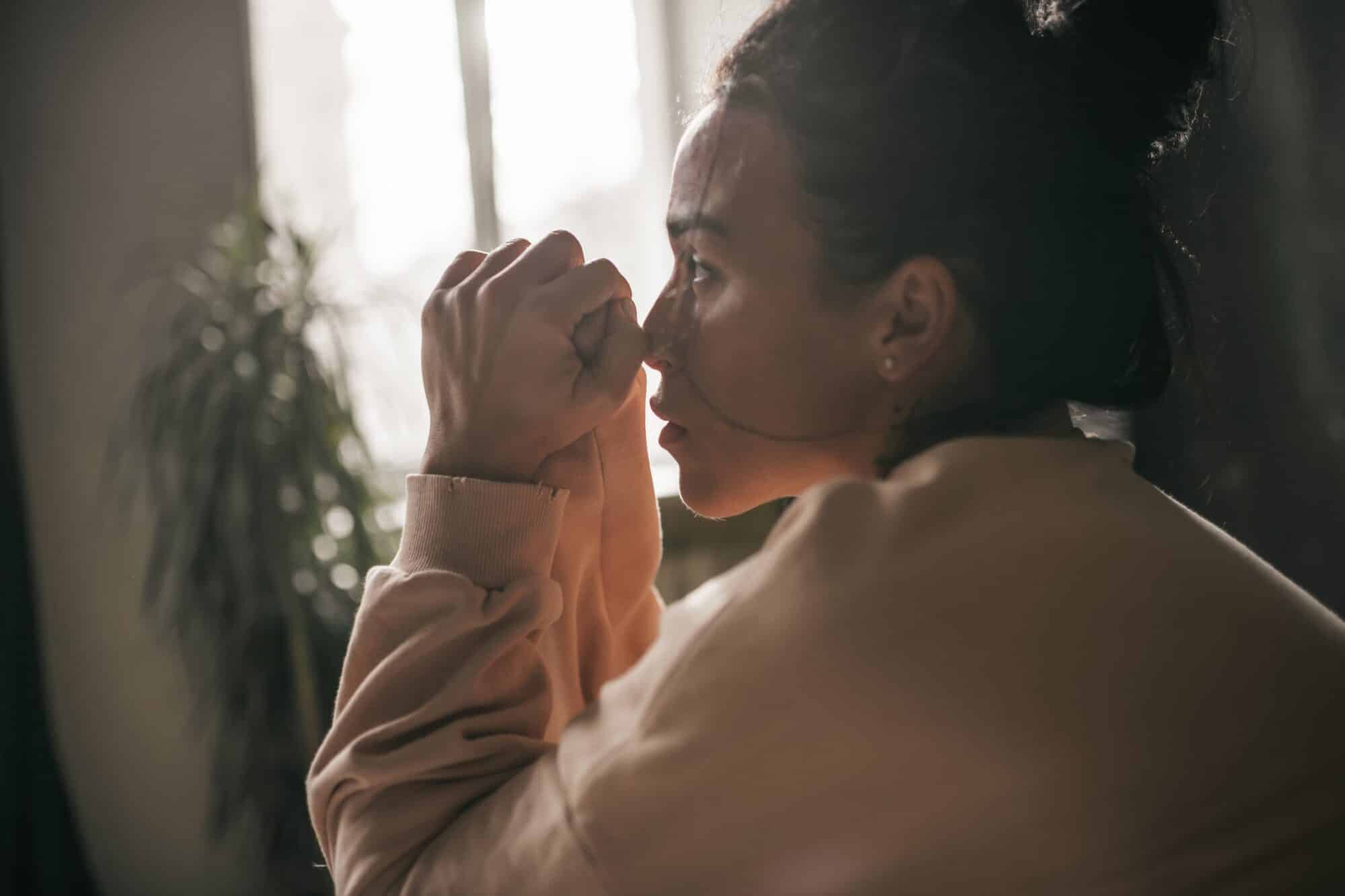 A woman sitting in a room looking stressed with her hands together for the topic dual diagnosis treatment center california.