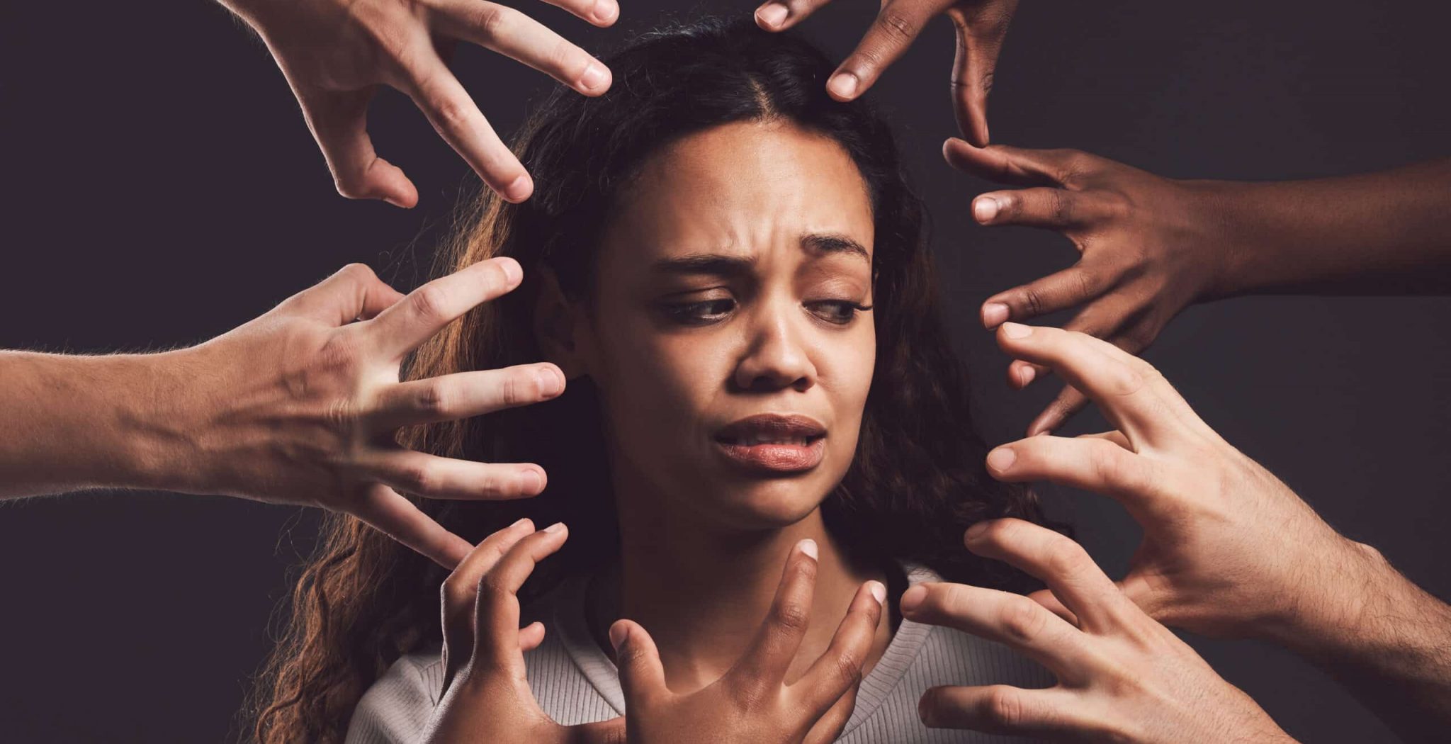 Shot of hands grabbing a young womans against a dark background.