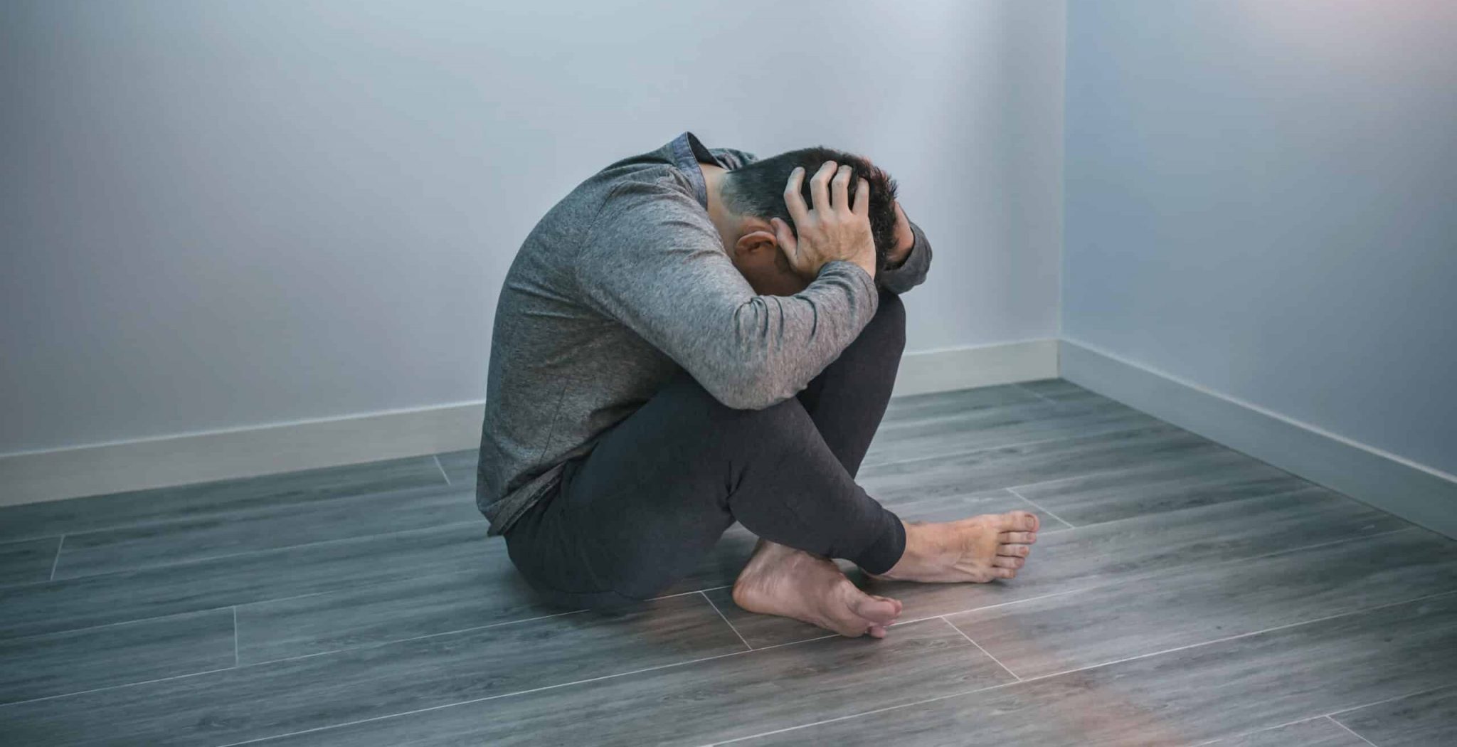 Unrecognizable man with problems holding his head with hands sitting on the floor. He has OCD and Trauma